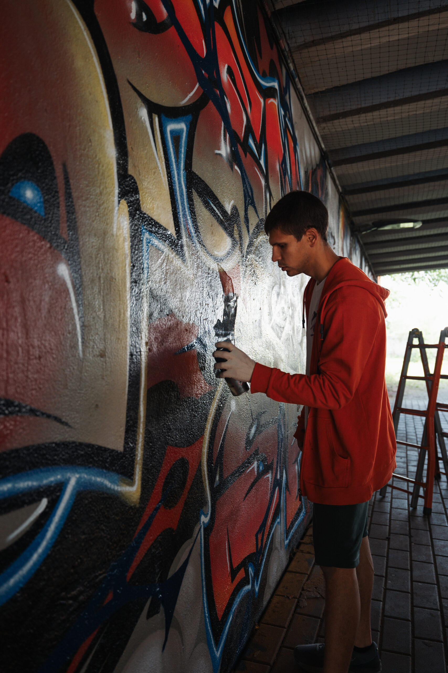 Un ragazzo sta realizzando un murales con una bomboletta. L'inquadratura è molto stretta e non permette di capire il soggetto del murales.