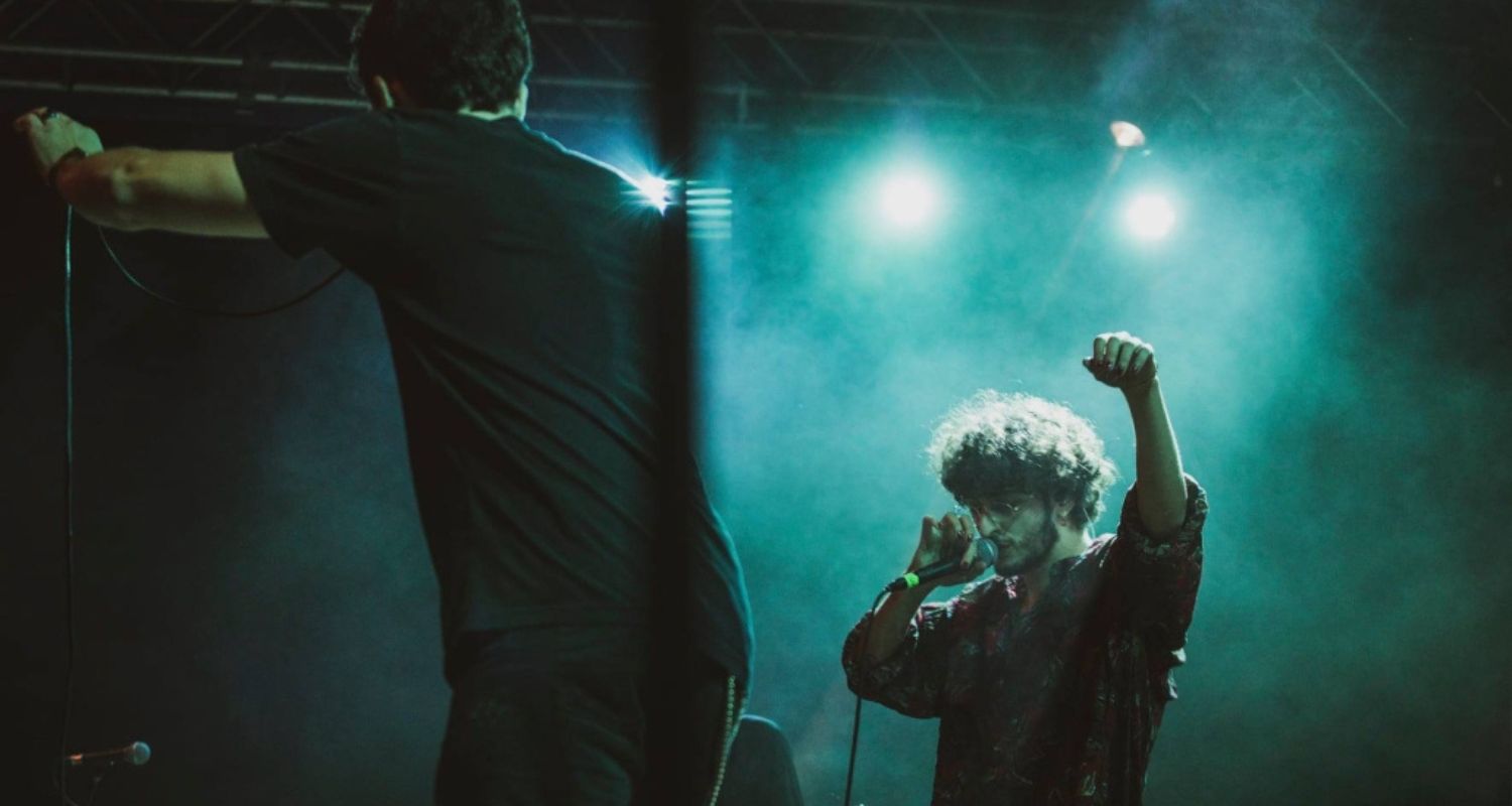 Due cantanti sul palco mentre cantano illuminati dai riflettori.