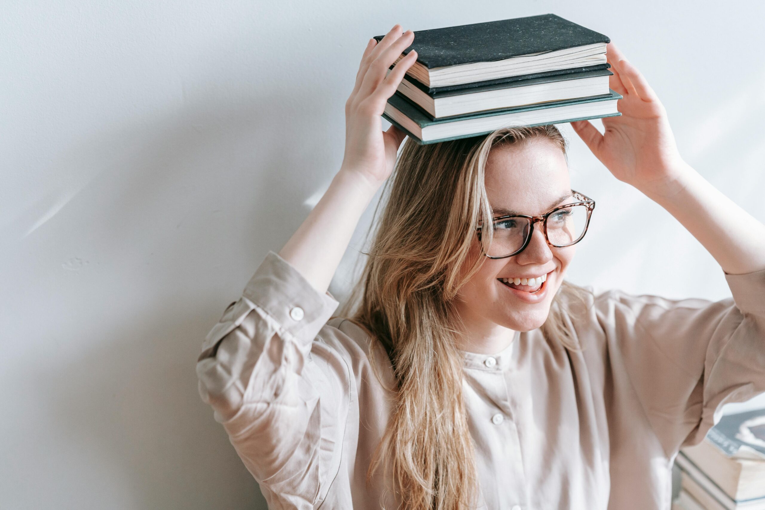 giovani con gli occhiali e un gruppo di libri sulla testa