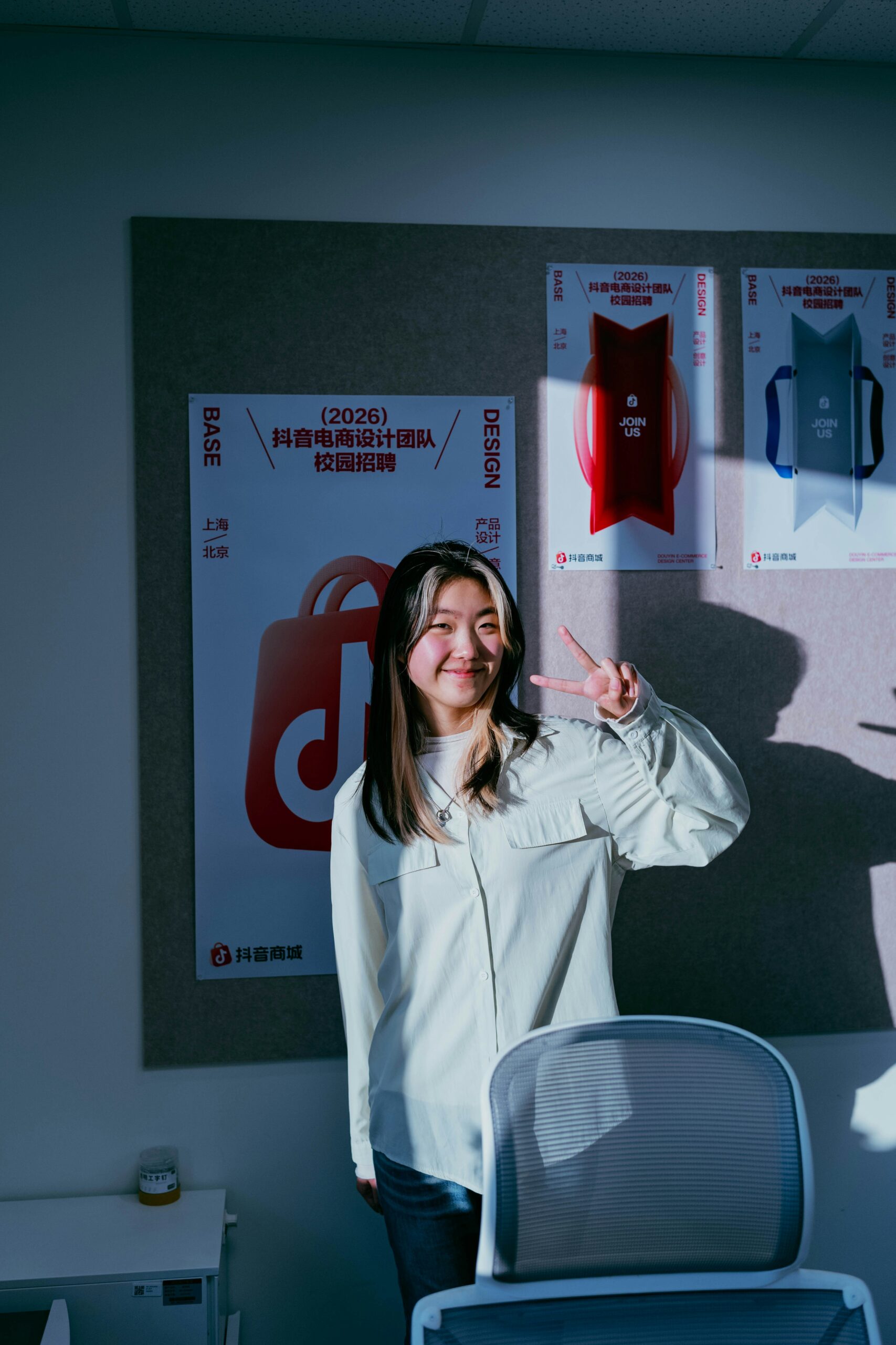 Giovane personain un ufficio, davanti a una bacheca con dei poster. Sorride e fa un gesto di evviva con la mano sinistra