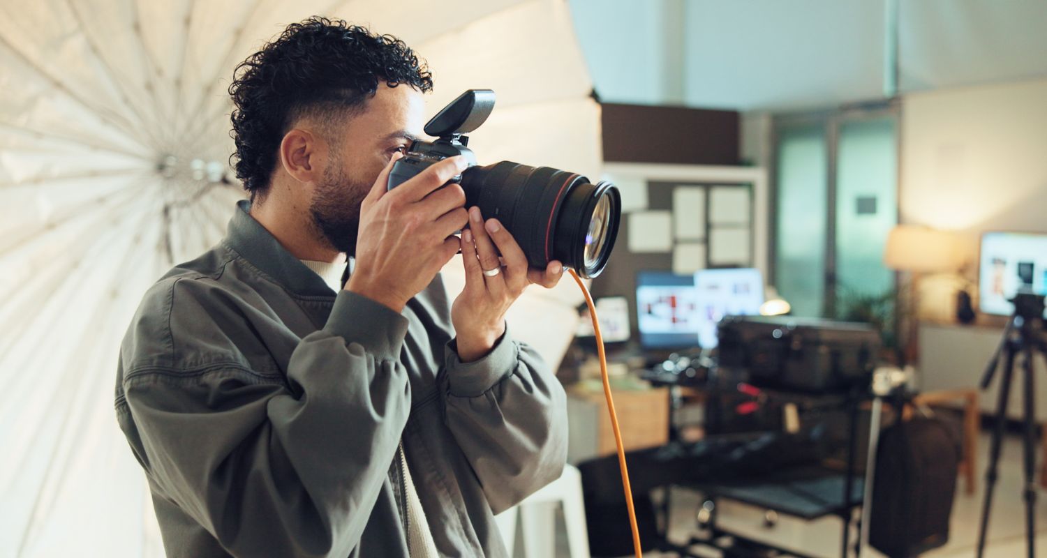 Un giovane fotografo scatta una fotografia in uno studio fotografico professionale, utilizzando una fotocamera reflex tra luci da set e attrezzatura per shooting.
