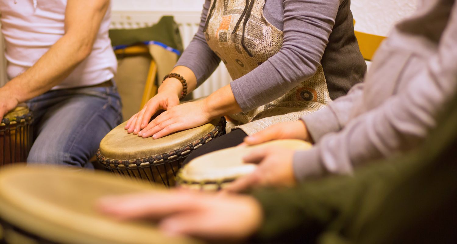 Gruppo di persone sedute in cerchio mentre suonano tamburi a percussione con le mani durante un'attività di Drum Circle. L'immagine mette in evidenza la partecipazione, la collaborazione e la condivisione attraverso la musica e il ritmo.