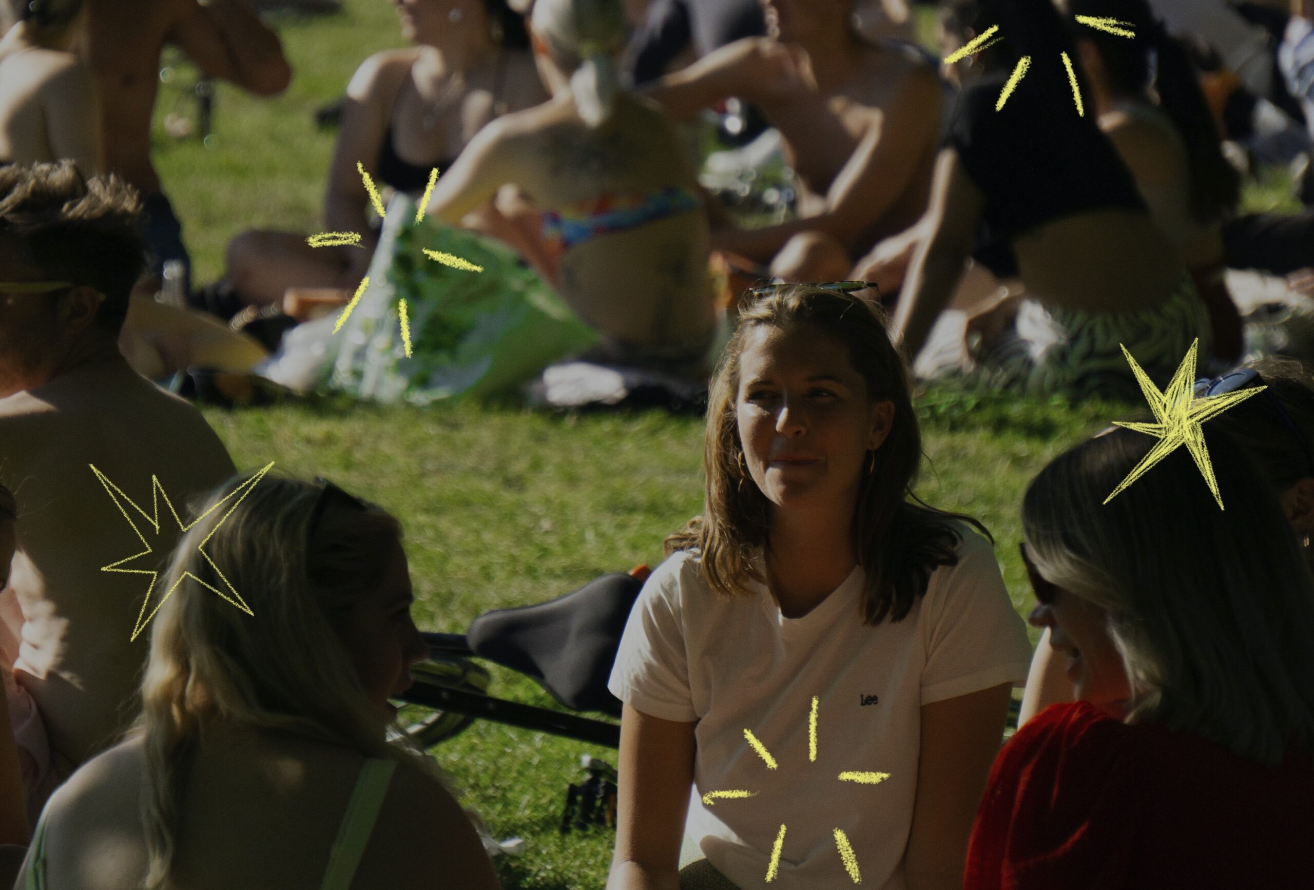 Gruppo di giovani seduti sull’erba durante un evento all’aperto in un parco, intenti a chiacchierare e socializzare in un’atmosfera informale e conviviale. Nell’immagine sono presenti elementi grafici decorativi a forma di stelle disegnate a mano.