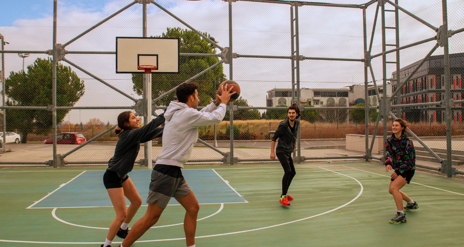 Gruppo di ragazze e ragazzi che giocano a basket su un campo all'aperto del Centro Sportivo R. Pilo durante un'attività dedicata ai giovani.