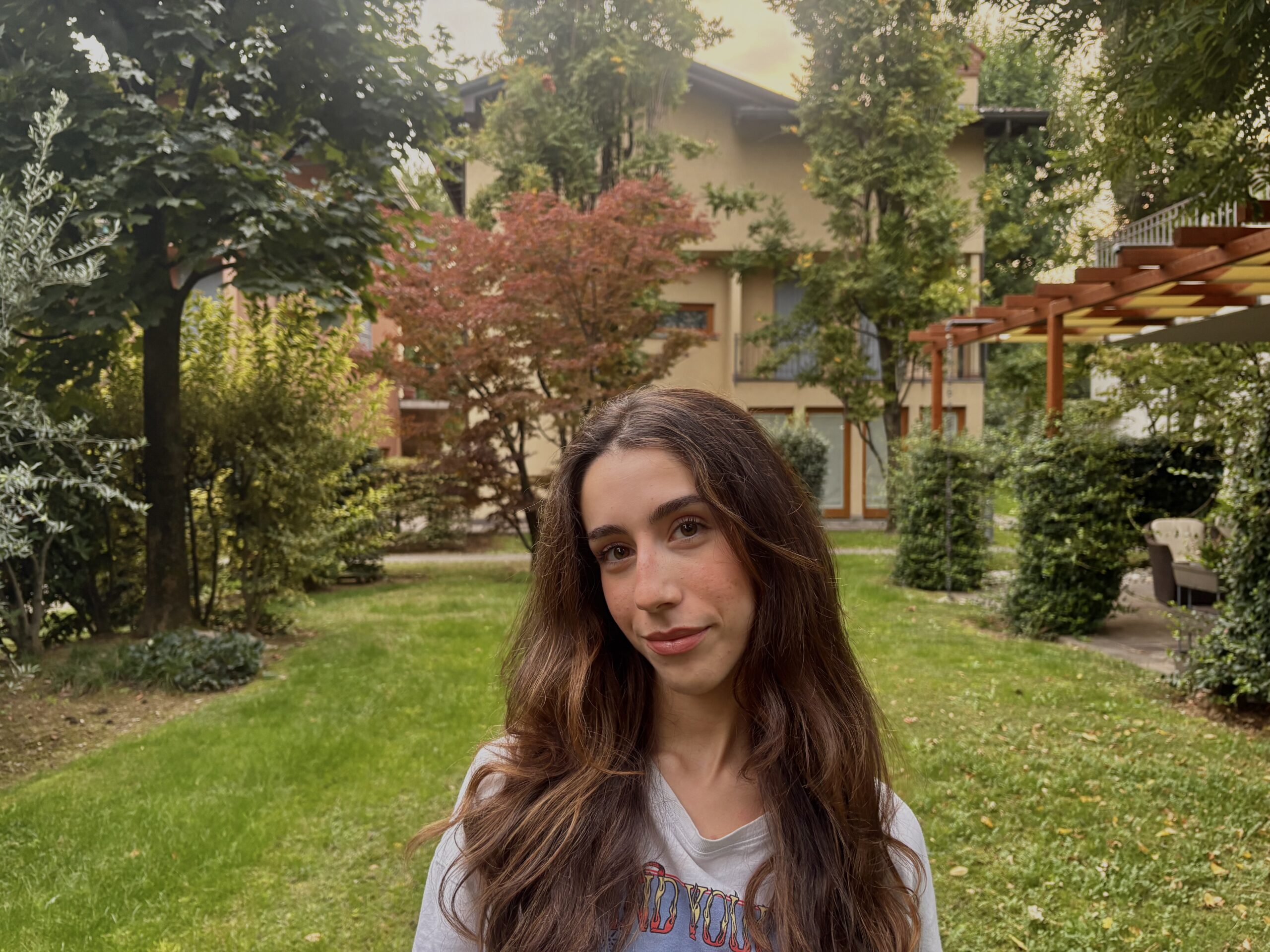 Carlotta ha i capelli lunghi e castano scuro. Ha gli occhi marroni. Indossa una felpa grigia e dietro di lei c'è lo sfondo di un parco con diversi alberi.